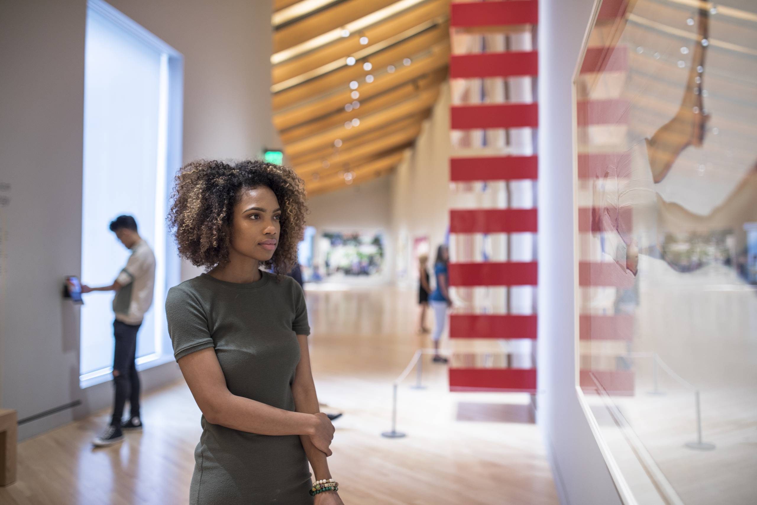 Woman looks at contemporary artwork Woman viewing art in a gallery with a wooden ceiling and a man in the background.