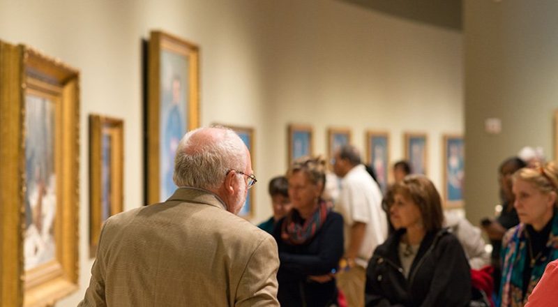 The Big Picture tour Group in art gallery viewing and discussing framed paintings on the walls.