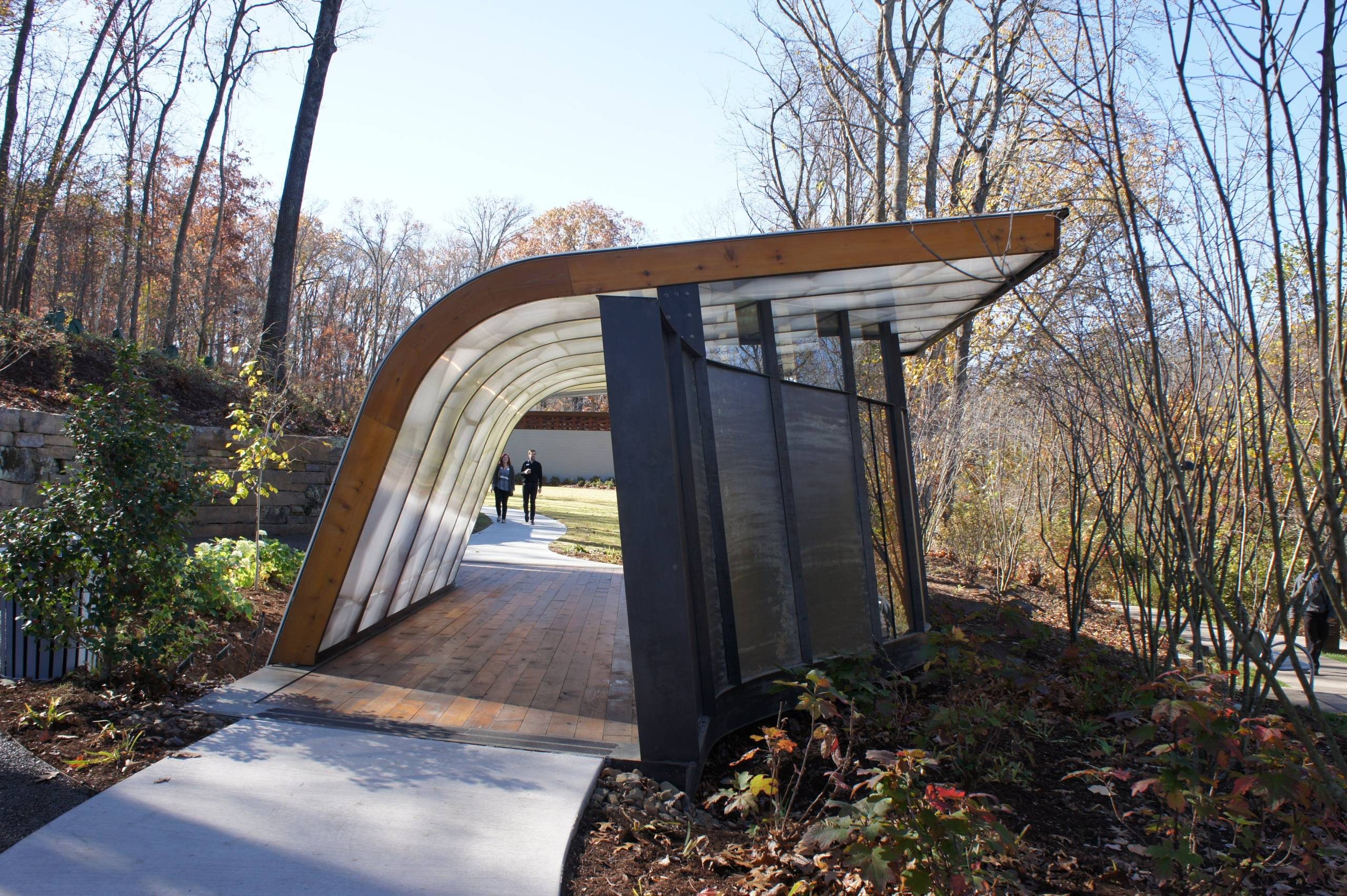 The Frank Lloyd Wright Welcome Pavilion Curved metal walkway in autumn woods with two people approaching along the path.
