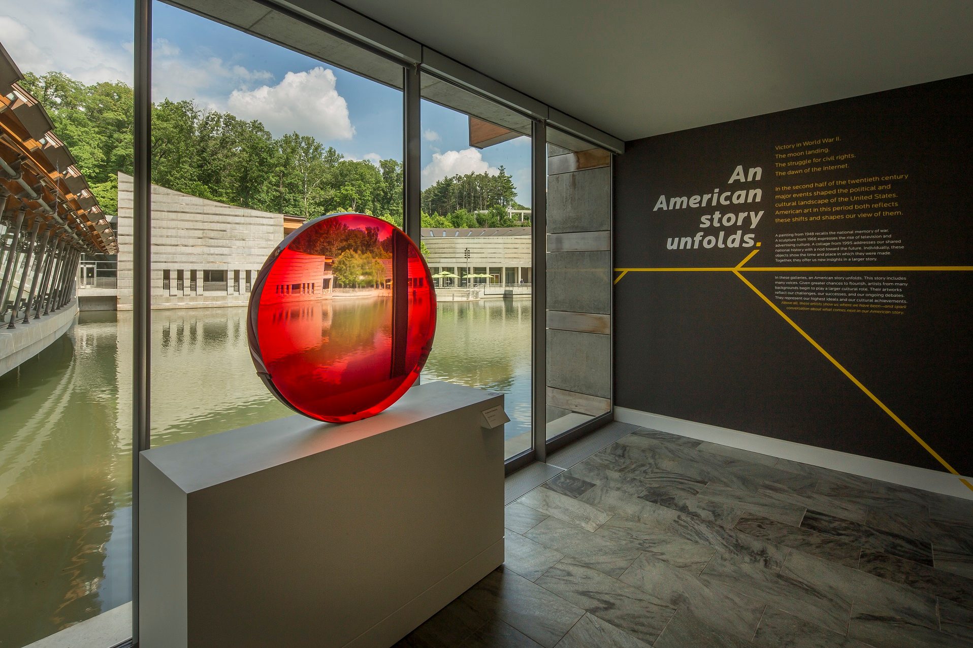 Fred Eversley, Big Red Lens, 1985, cast polyester, 40 × 40 × 6 in. (101.6 × 101.6 × 15.2 cm). Crystal Bridges Museum of American Art, Bentonville, Arkansas, 2010.66. Interior with large windows, red glass sculpture, modern building, and American history text.