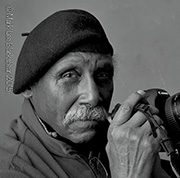 headshot-cowans-adger-1 Elderly man in beret holding a camera, black and white portrait.