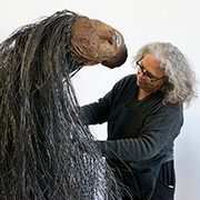 headshot-saar-alison Person crafting large horse-like sculpture with fibrous materials indoors