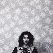 headshot-smith-ming Person with curly hair holding a camera, floral wallpaper, black and white image.