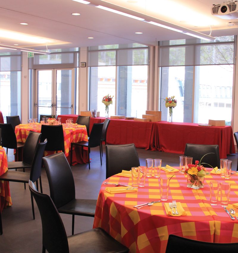 Luncheon Banquet room with checkered tablecloths, set tables, black chairs, and buffet near large windows.