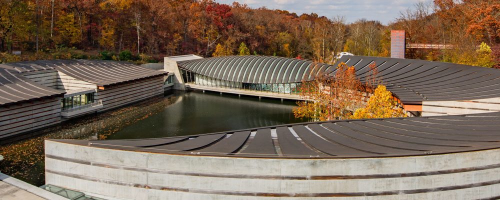 Fall at Crystal Bridges Modern complex with curved roofs, central water body, and surrounding autumn forest.