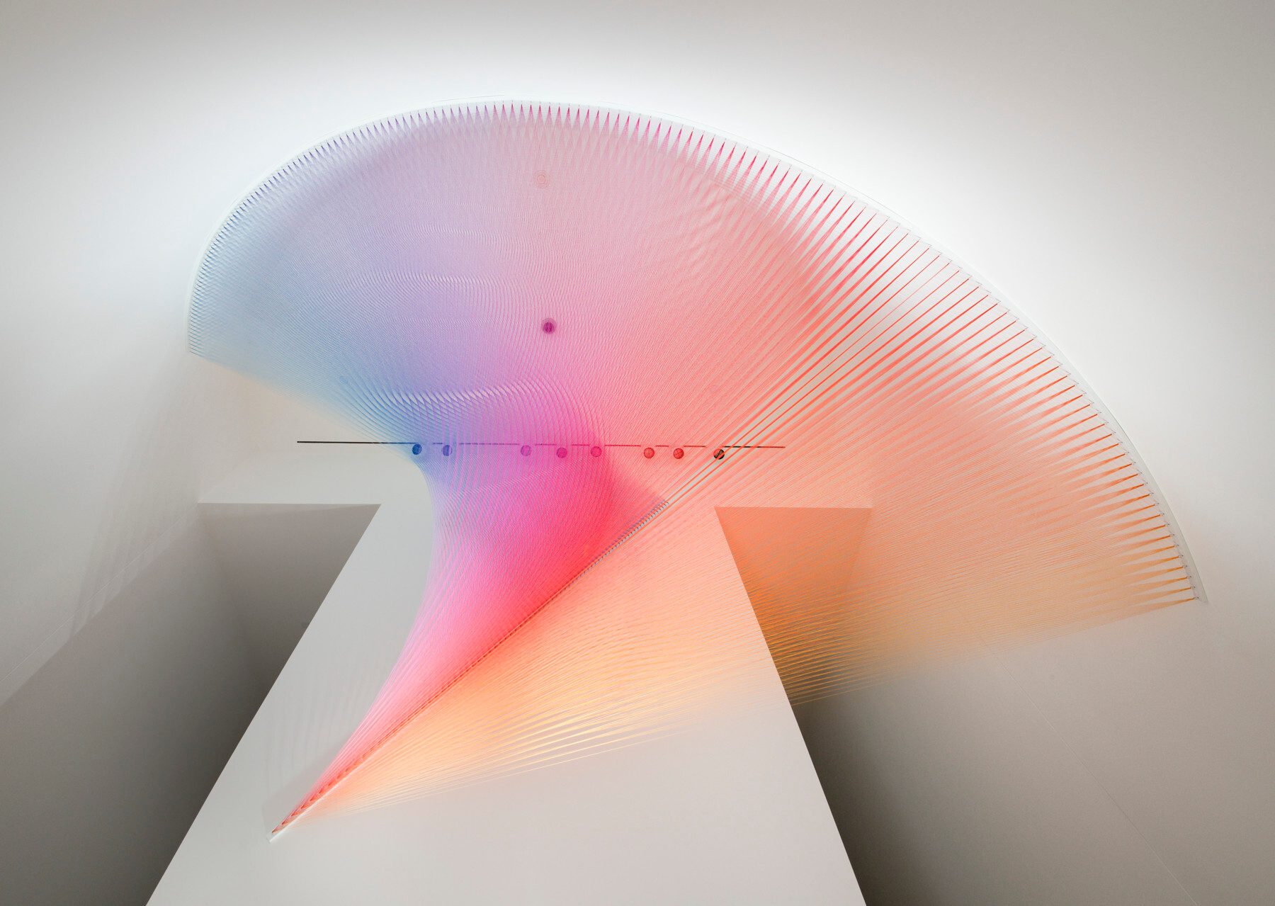 Gabriel Dawe, Plexus No. 27, 2014, thread and steel hooks, 120 in. × 132 in. × 20ft. Crystal Bridges Museum of American Art, Bentonville, Arkansas, 2015.30 Colorful strings form a sweeping arc in a modern space, creating a blue, pink, and orange gradient.