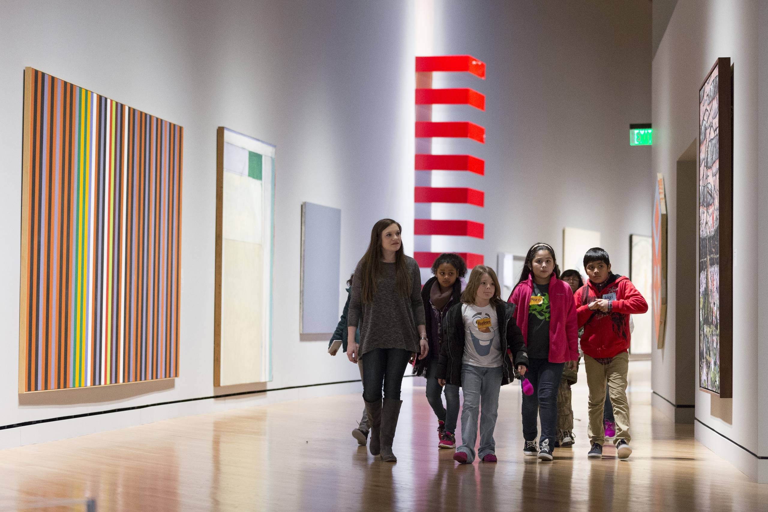 SDALE SCHOOLS TOUR Children and an adult exploring a modern art gallery hallway with colorful abstract paintings.
