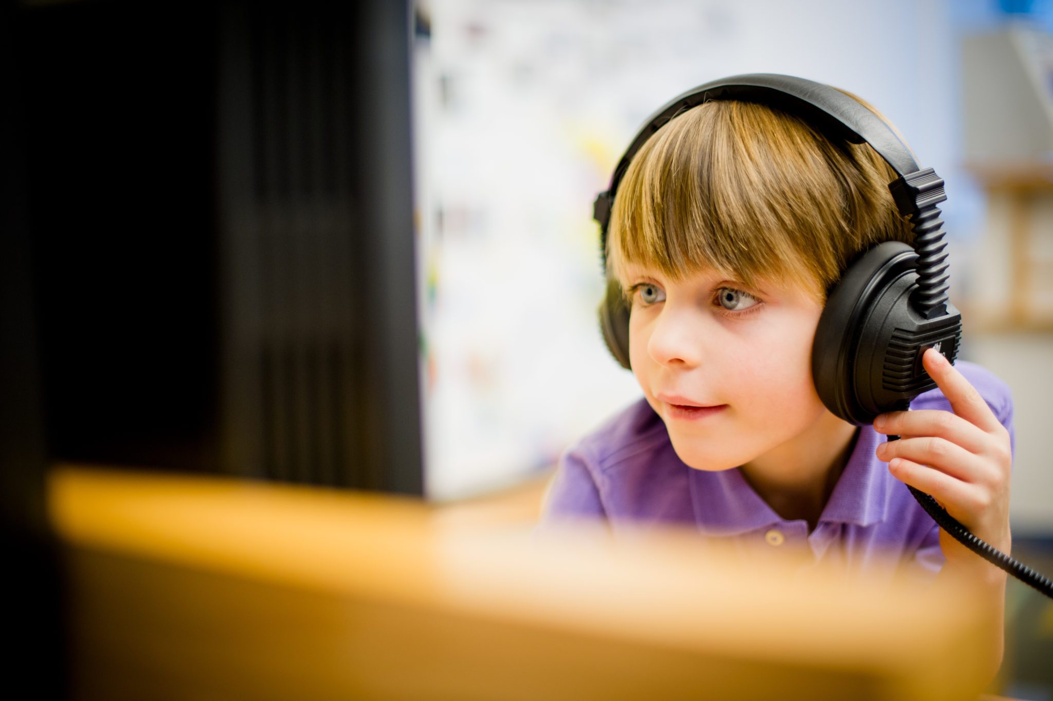 The Studio Child with large headphones looking at a computer screen in a bright indoor setting.