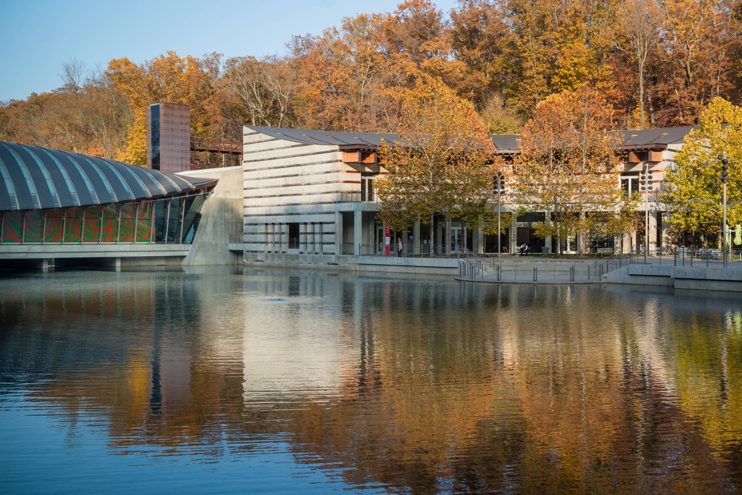 Fall at Crystal Bridges Modern building with large glass windows by a reflective lake, surrounded by autumn trees.