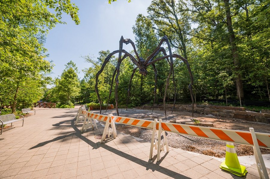 Louise Bourgeois, Maman, 1999, bronze, stainless steel, and marble, 30ft. 5 in. × 29ft. 3 in. × 33ft. 7 in. Crystal Bridges Museum of American Art. Now located on the South Lawn near the Twin Bridges. Photo by Ironside Photography / Stephen Ironside. Outdoor area with large spider sculpture, trees, benches, barricades, and caution tape.
