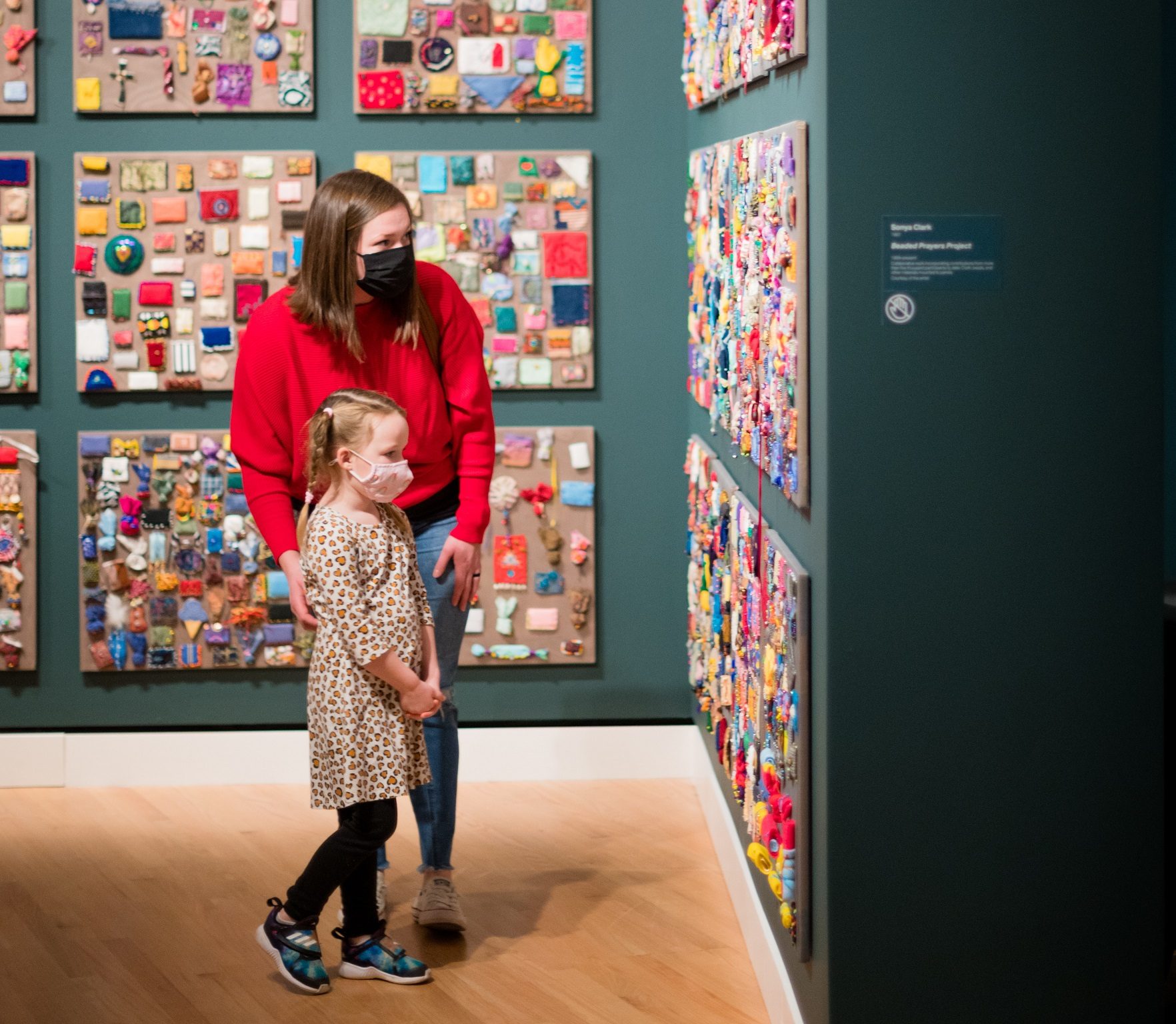 Guests in Crafting America gallery Woman and girl wearing masks viewing colorful wall art in a well-lit gallery.