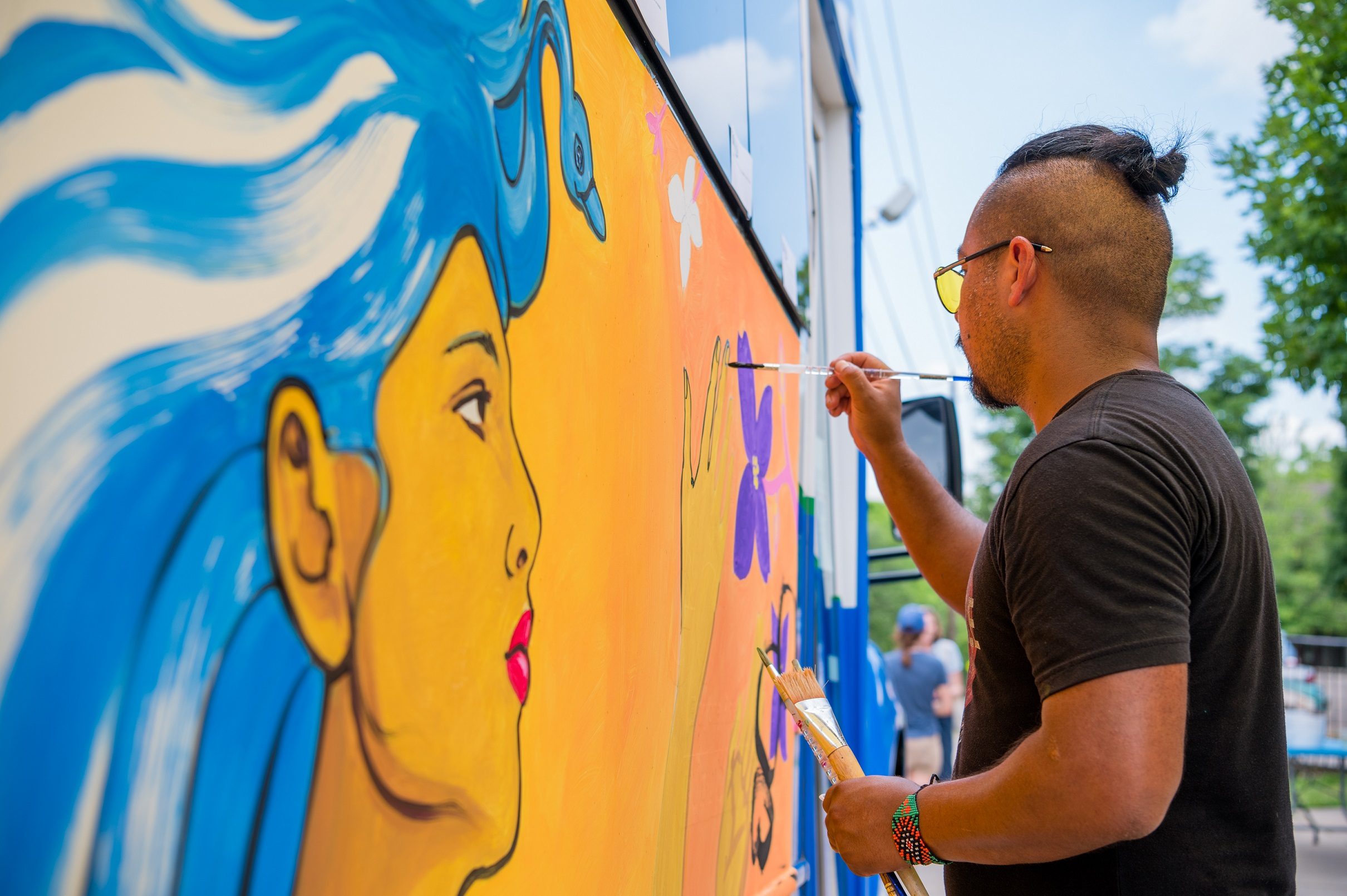 Octavio Logo paints the side of a bus at the Where To event. Photo by Ironside Photography / Stephen Ironside. Community event in fayetteville as an artist paints on a bus