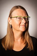 symposium-hs-doss-erica Person with long hair and glasses, facing slightly sideways against a neutral background.