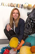 symposium-hs-longobardi-pam Person with long hair in dark blazer crouching among colorful buoys and maritime objects.