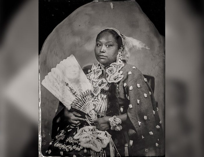 wilson-will-small Person in intricate attire with fan, adorned with detailed designs and textures, seated for portrait.